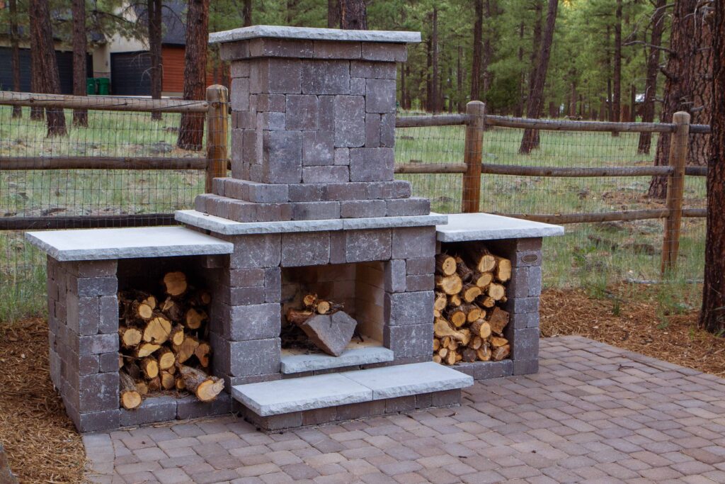 Outdoor large fireplace on an block patio with chopped wood sitting in the fireplace
