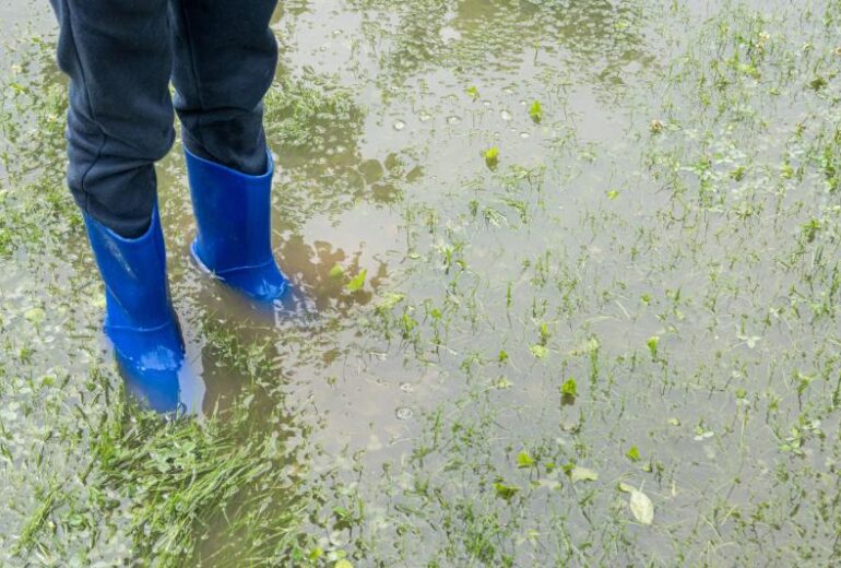 person in blue rain boots standing in flooded yard